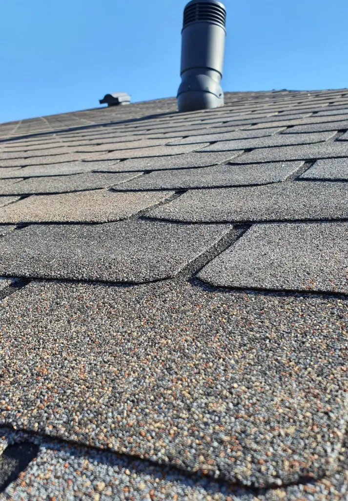 A close view of an asphalt shingle roof with a vent pipe under a blue sky
