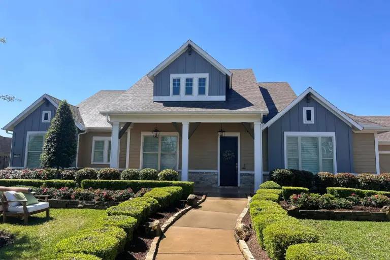 A blue gray craftsman style home with white trim, clipped hedges and a front walkway