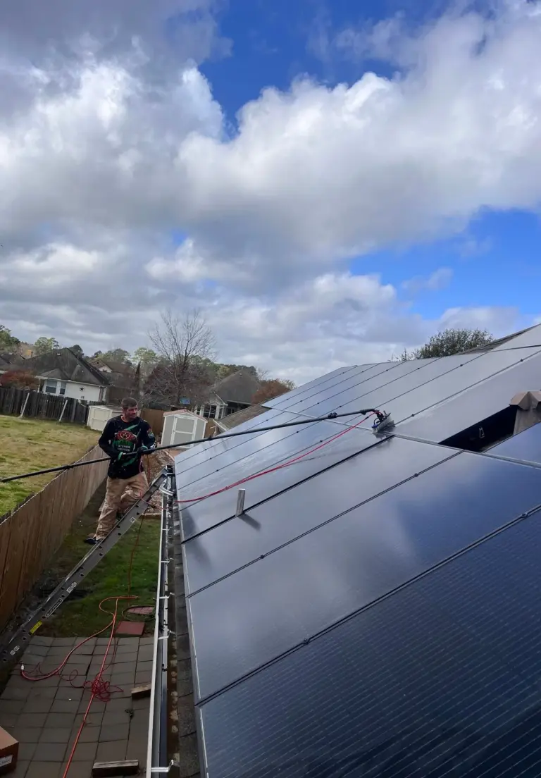 A worker cleaning a solar array with a water fed pole brush in a back yard
