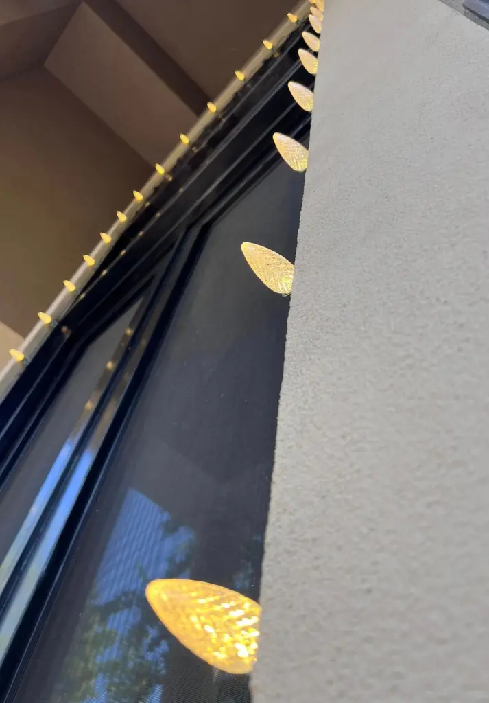 Close-up of warm white C9 Christmas bulbs lining the stucco wall and eave of a home