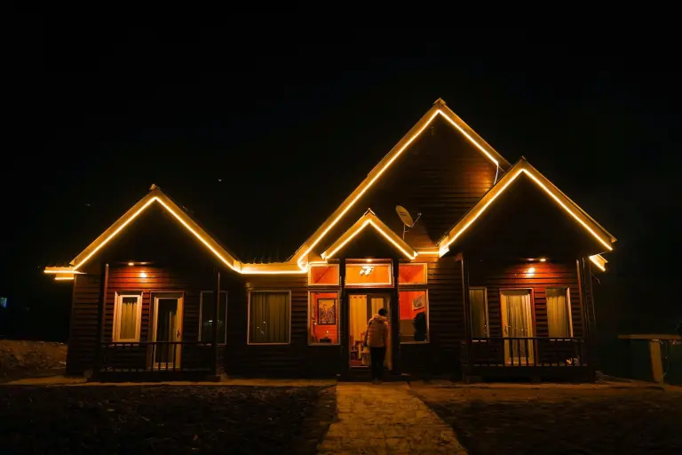 Warm Christmas lights outlining the gables and roofline of a dark wood-sided building at night