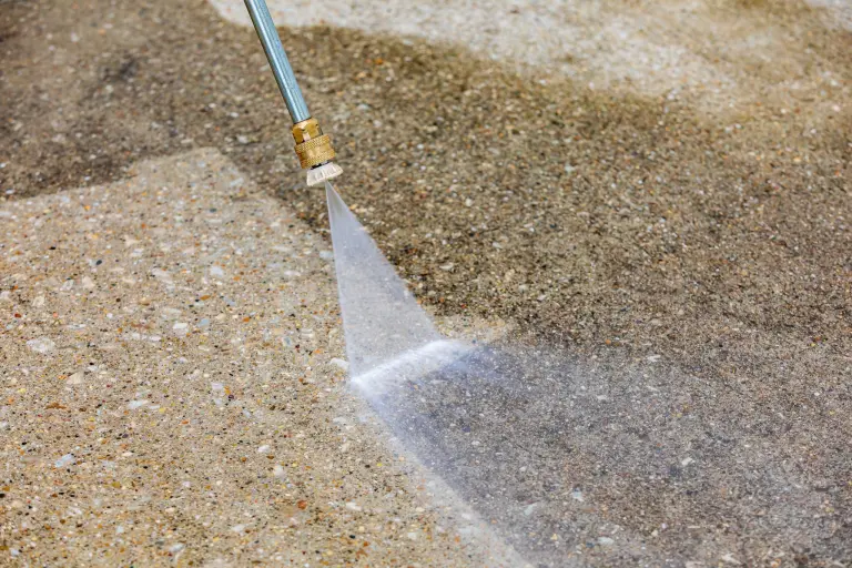 A pressure washer leaving a clean stripe across an aggregate driveway