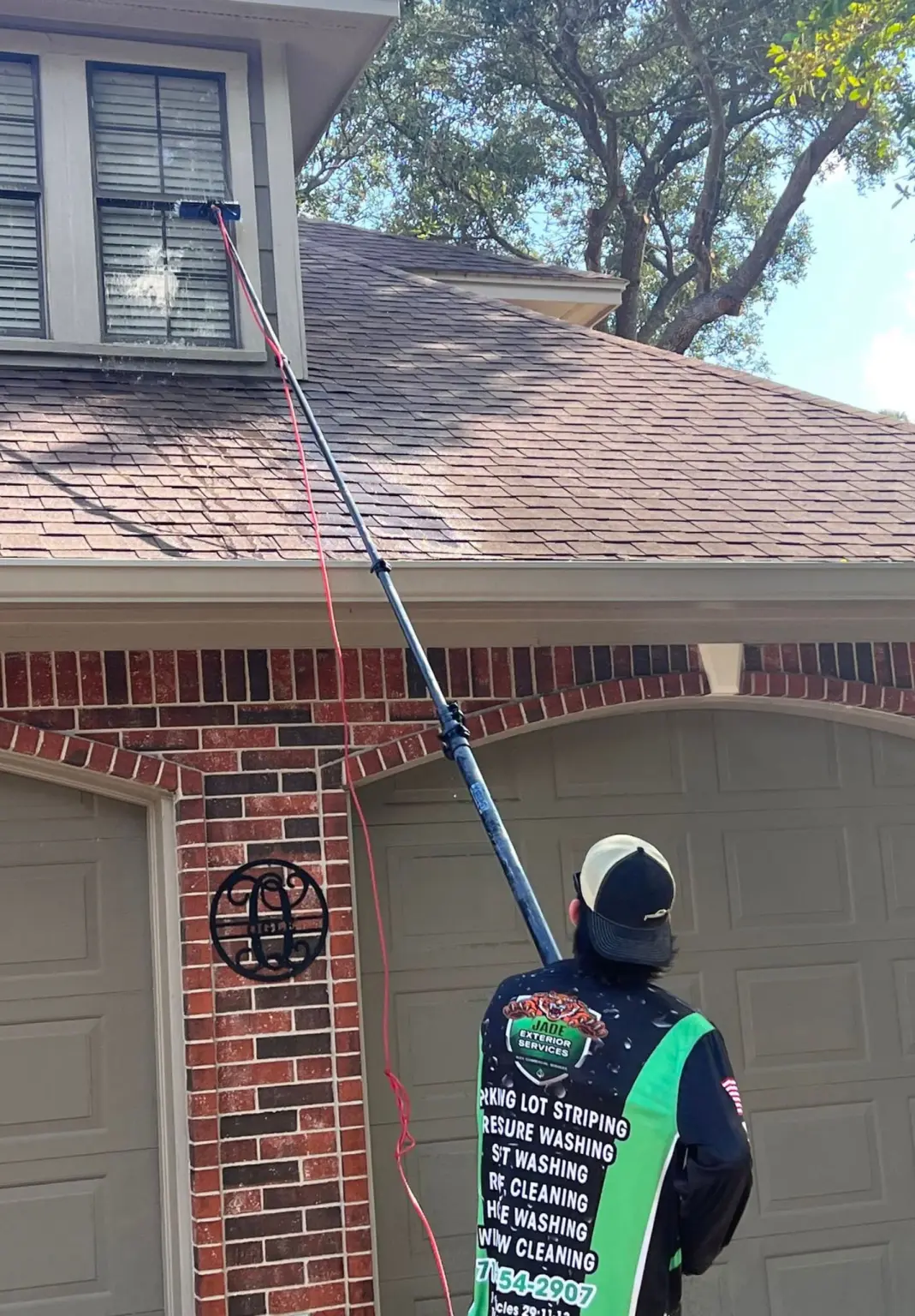 A Jade technician cleaning a second story window with a water fed pole on a brick home