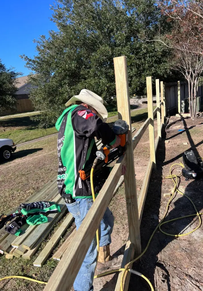 A crew member nailing new rails onto fresh posts for a wood fence