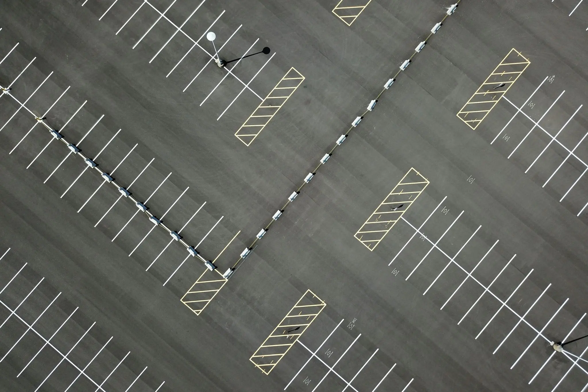 An overhead view of a parking lot with white stall lines and yellow hatched no parking areas