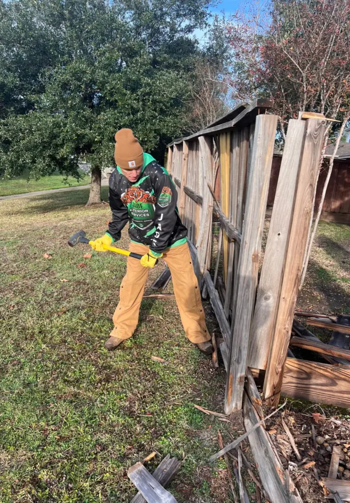 A crew member pulling boards off an old wood privacy fence with a pry bar