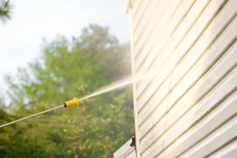 Rinsing cream colored lap siding with a spray wand during a house wash