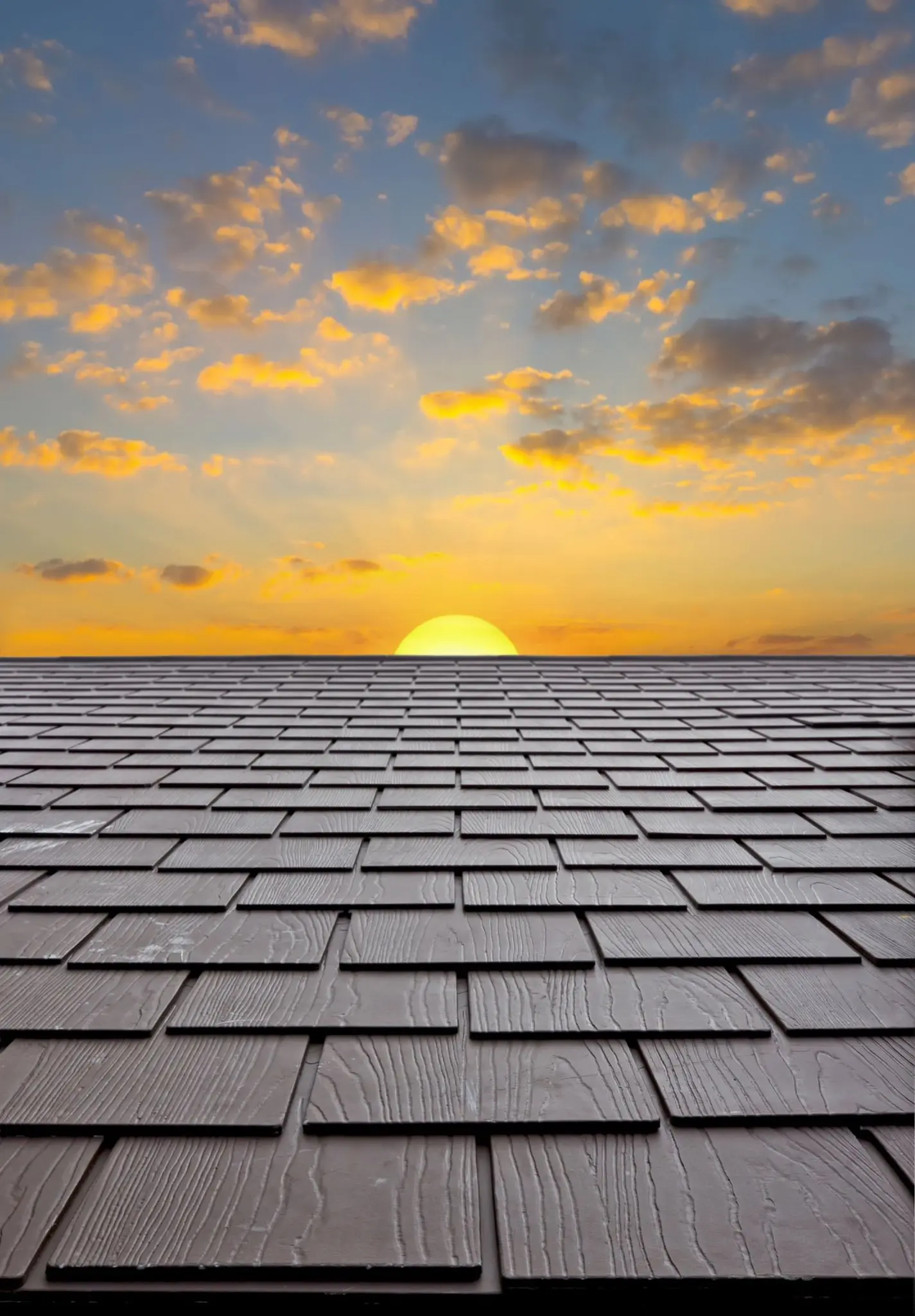 A shingle roof silhouetted against an orange sunrise sky