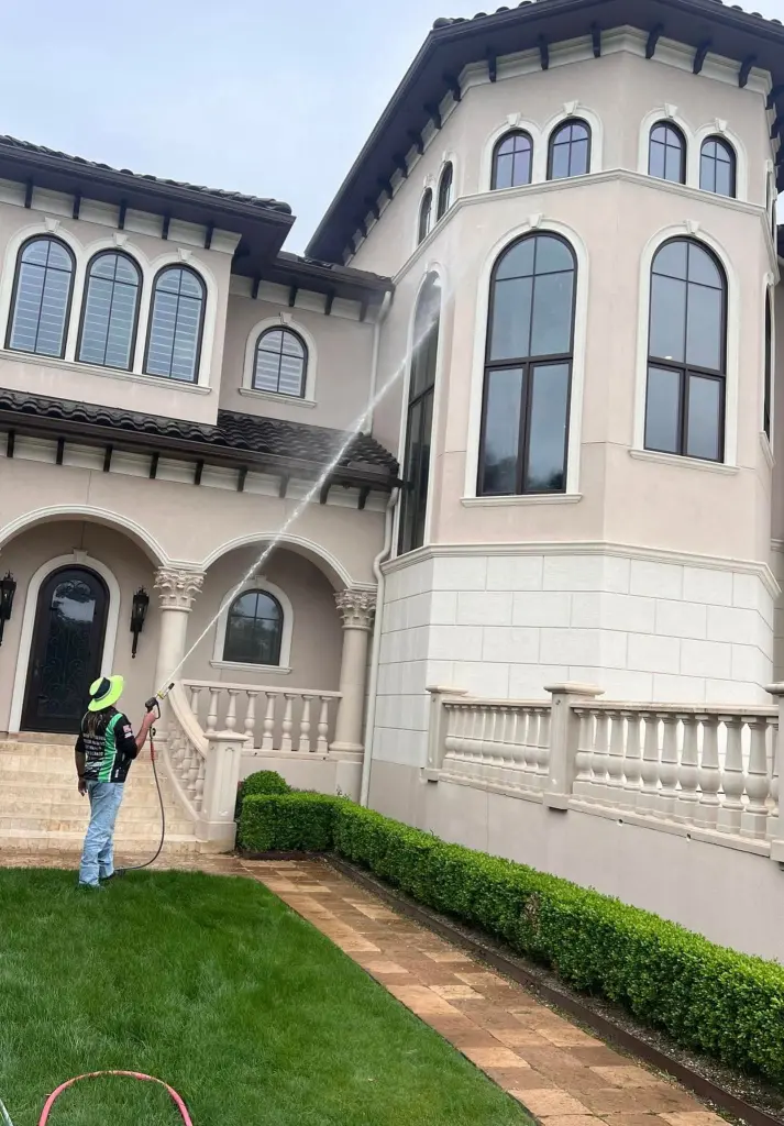 A Jade technician soft washing the front of a tan Mediterranean style home with arched windows