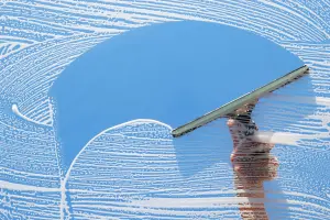 A squeegee wiping a soapy window with blue sky showing through the clean glass
