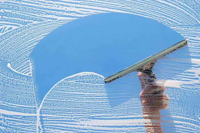 A squeegee wiping a soapy window with blue sky showing through the clean glass