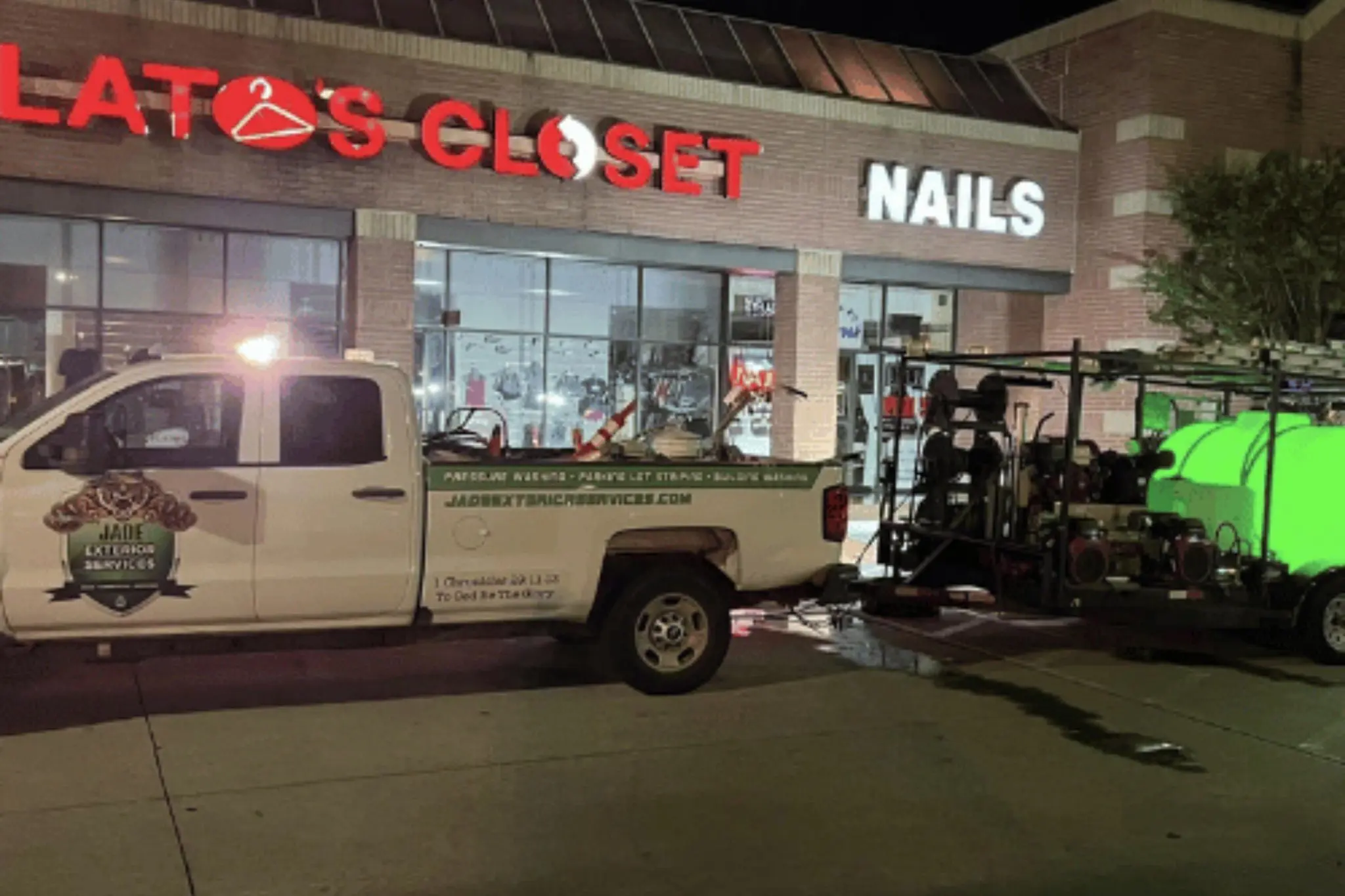 A Jade truck and pressure washing trailer parked outside a strip center storefront at night