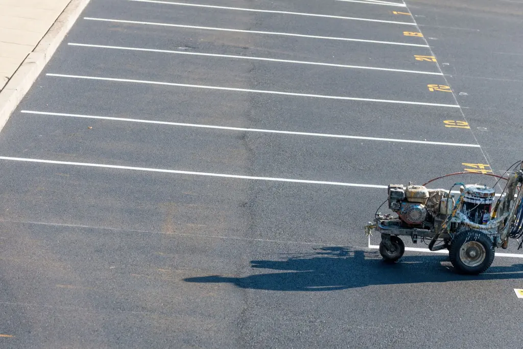 A line striping machine painting fresh white lines and numbered stalls on an asphalt lot
