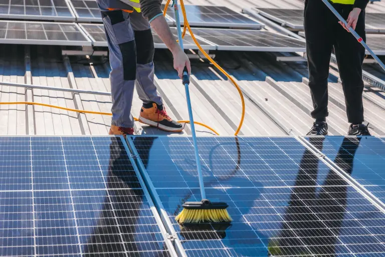 Two workers washing solar panels with brushes and a water hose