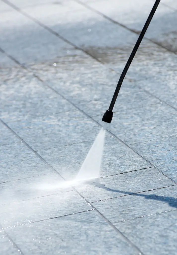 A pressure washer nozzle cleaning gray paving slabs