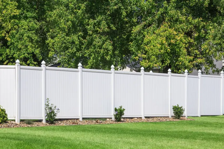 A white vinyl privacy fence running along a mowed lawn with trees behind it